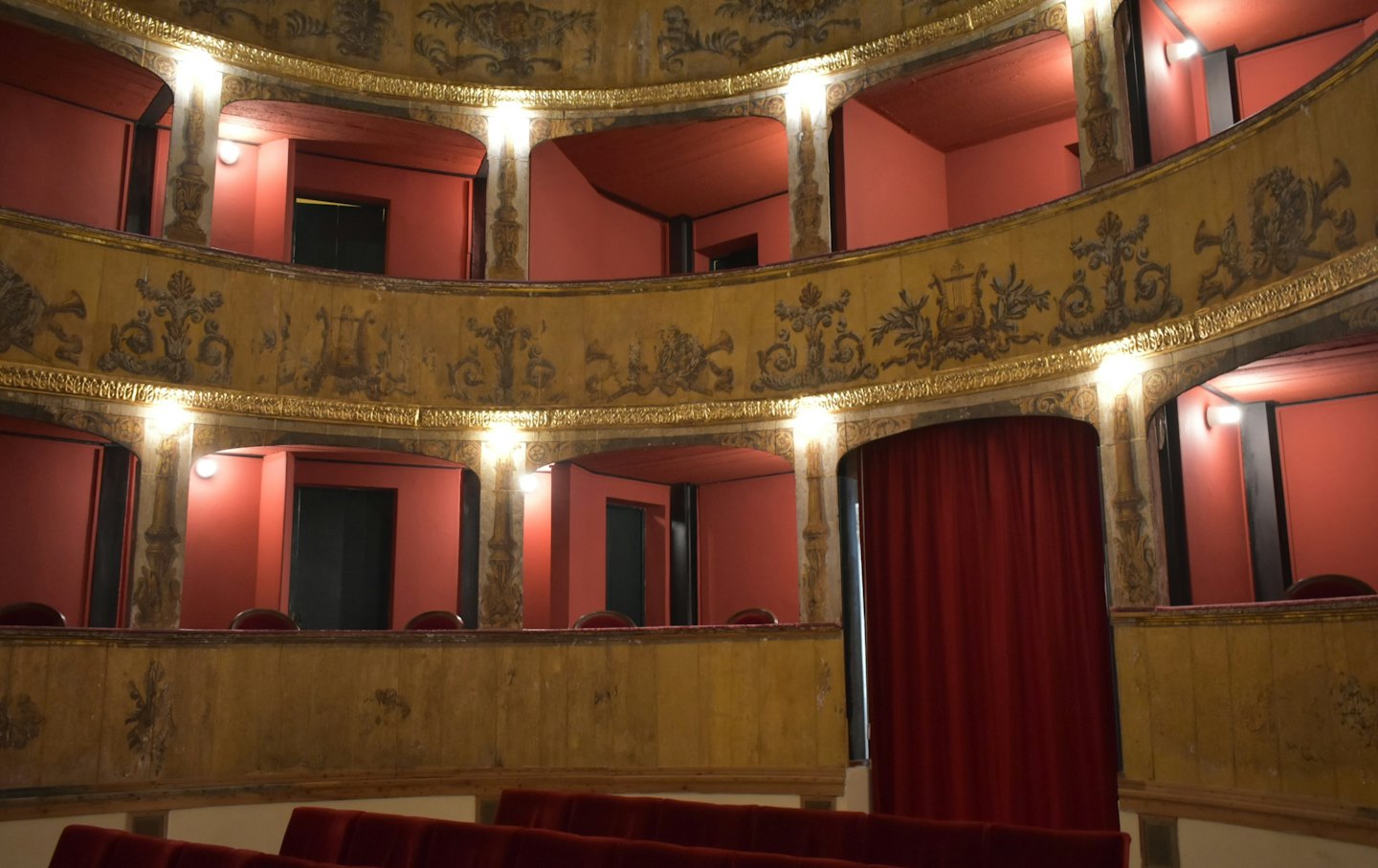 Interno di un teatro storico vuoto con balconi decorati e sedili in velluto.