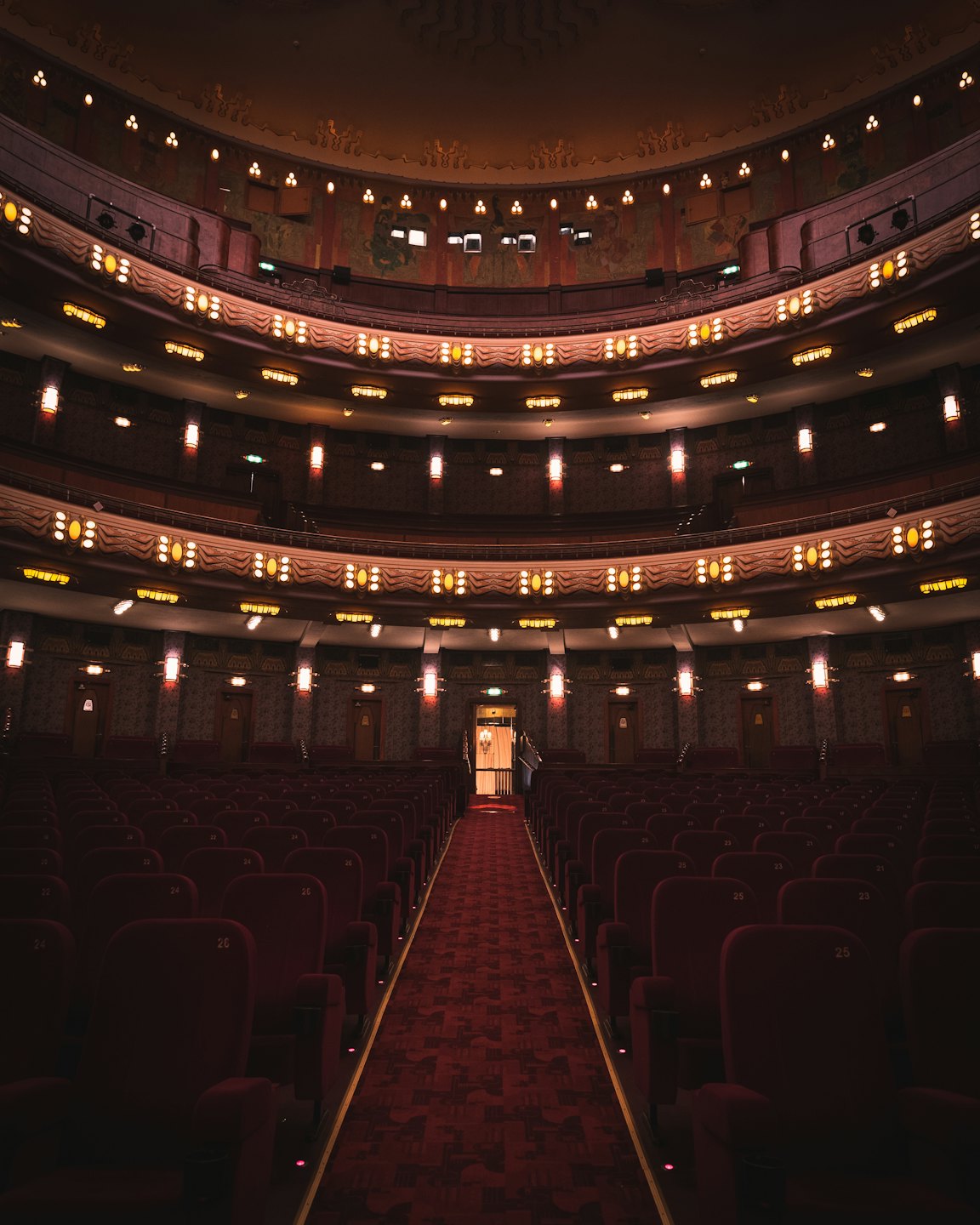 Teatro vuoto e sontuoso con poltrone di velluto rosso e balconi illuminati.